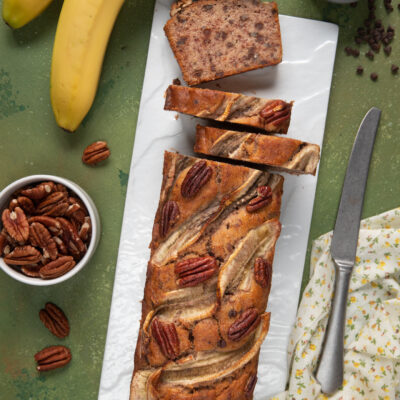 Banana bread vegano affettato con banane caramellate in superficie, noci pecan e gocce di cioccolato