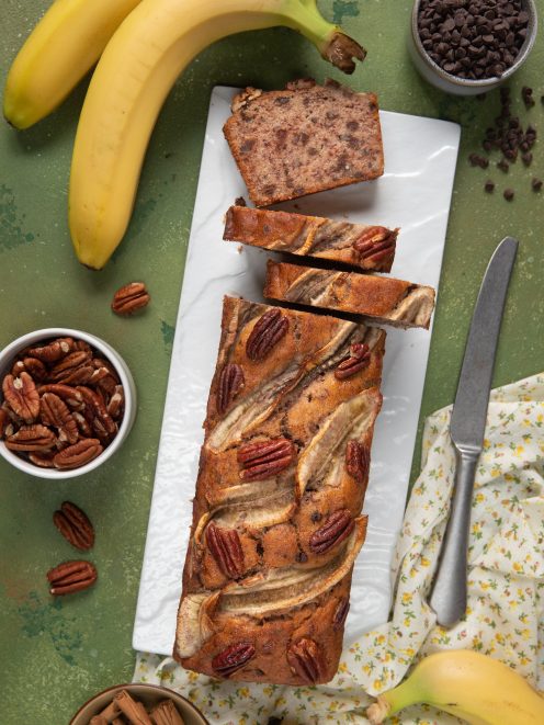 Banana bread vegano affettato con banane caramellate in superficie, noci pecan e gocce di cioccolato