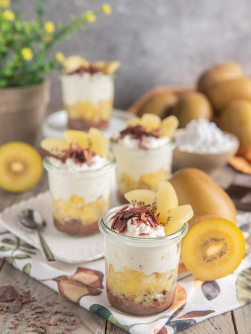 Bicchierino con yogurt, cioccolato e kiwi giallo a strati, guarnito con scaglie e fette fresche