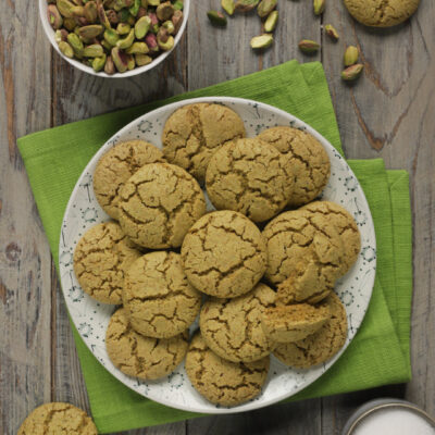 Biscotti al pistacchio dorati e incrinati in superficie, serviti su un piatto con pistacchi sgusciati accanto