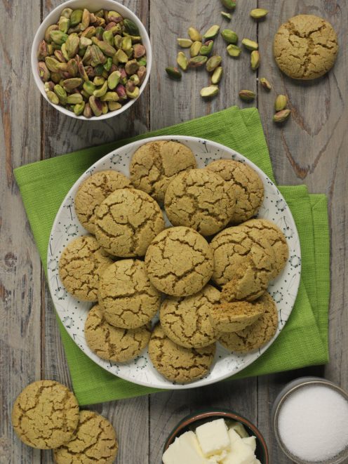 Biscotti al pistacchio dorati e incrinati in superficie, serviti su un piatto con pistacchi sgusciati accanto