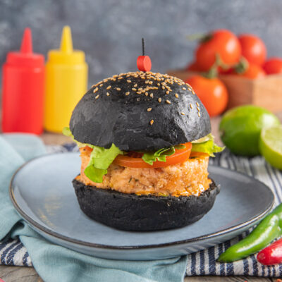 Burger di salmone con bun al carbone vegetale, lattuga, pomodoro e salsa piccante