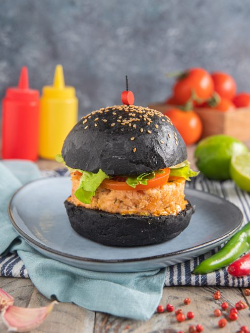 Burger di salmone con bun al carbone vegetale, lattuga, pomodoro e salsa piccante