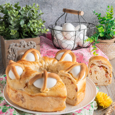 Casatiello napoletano a ciambella con uova intere incastonate nella superficie dorata e una fetta che mostra il ripieno