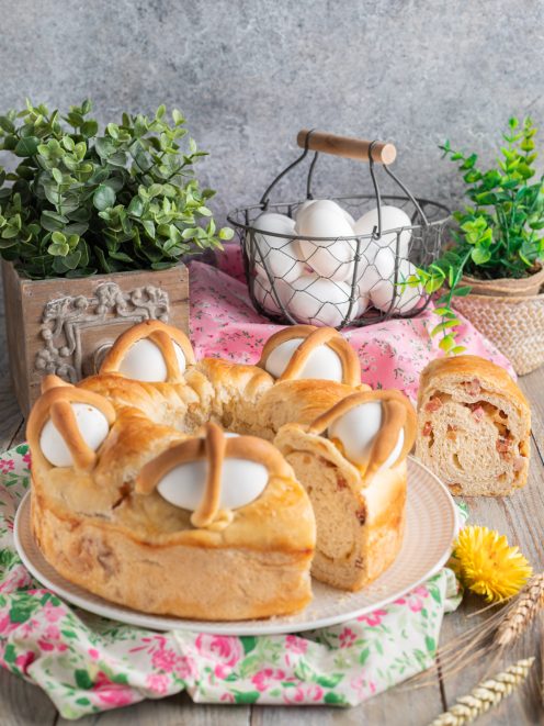 Casatiello napoletano a ciambella con uova intere incastonate nella superficie dorata e una fetta che mostra il ripieno