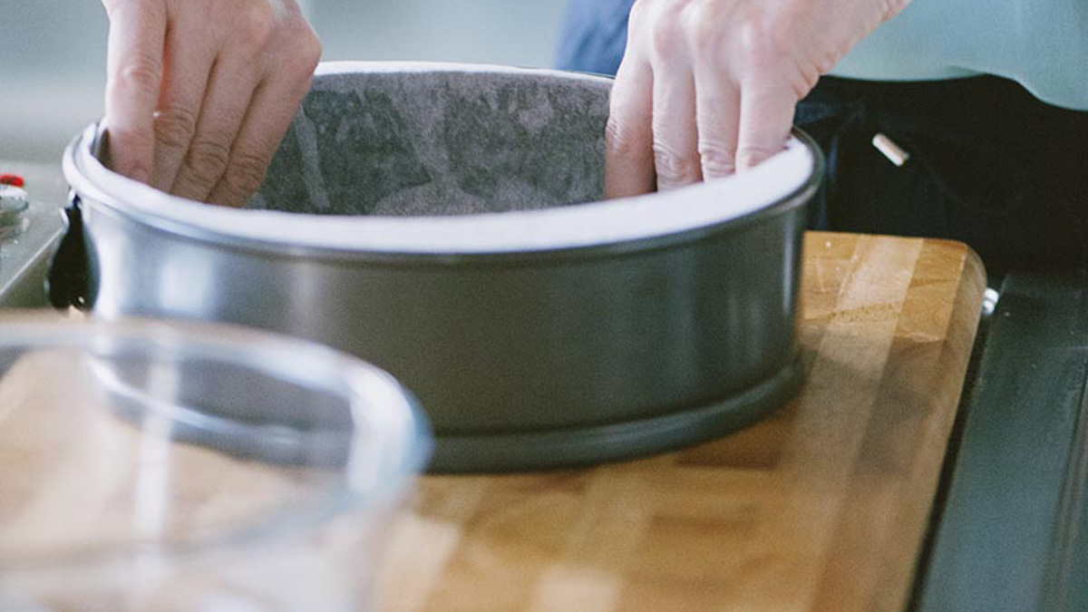 Mani che foderano con carta da forno una tortiera a cerchio apribile