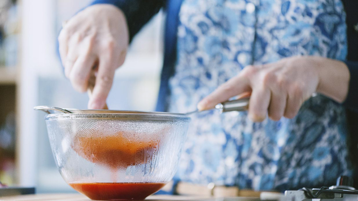 Salsa di fragole setacciata attraverso un colino a maglie strette con una spatola