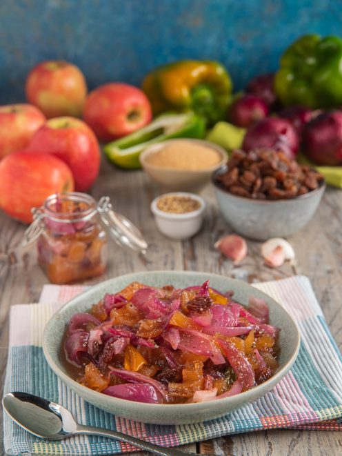 Chutney di mele, cipolle e zenzero in ciotola con uvetta e peperoni sullo sfondo