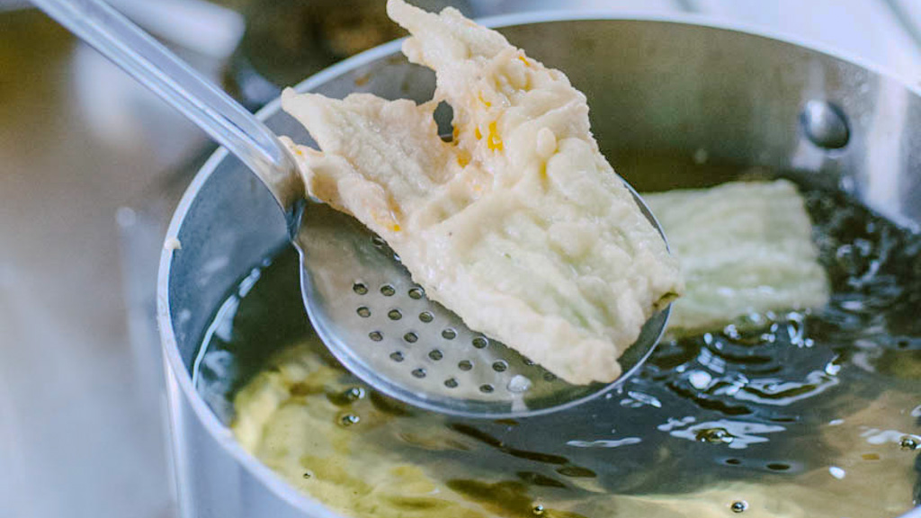 Fiore di zucca in pastella sollevato dall'olio bollente con un mestolo forato