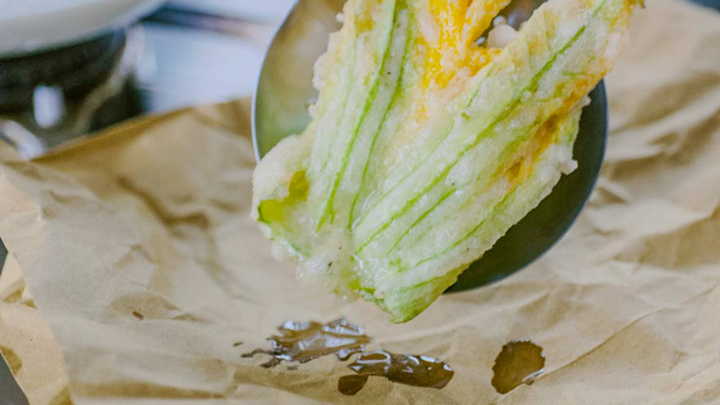 Fiore di zucca in pastella scolato su carta assorbente con olio che cola