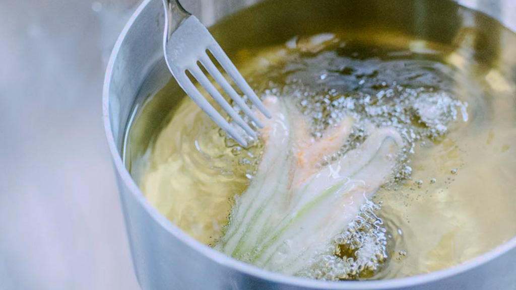 Fiore di zucca immerso nell'olio bollente sorretto da una forchetta