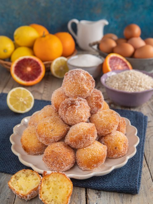 Frittelle di riso di San Giuseppe impilate a piramide zuccherate, con una tagliata a meta' che mostra l'interno soffice