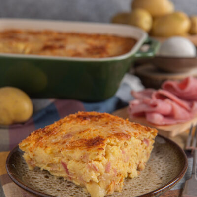 Gateau di patate con prosciutto cotto e formaggio filante, servito a fetta con crosta dorata