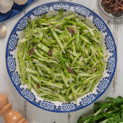 Insalata di puntarelle alla romana con filetti di acciuga condita e servita in un piatto da portata