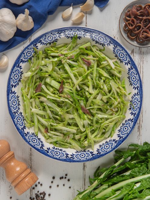 Insalata di puntarelle alla romana con filetti di acciuga condita e servita in un piatto da portata