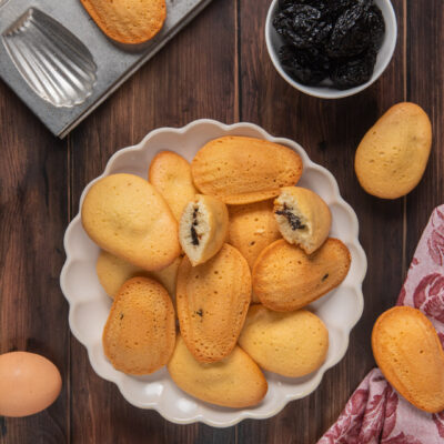 Madeleines con cuore di prugne accatastate in una ciotola, alcune spezzate a mostrare il ripieno
