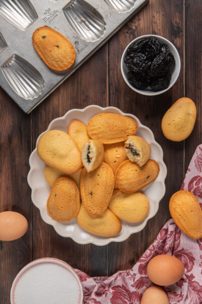 Madeleines con cuore di prugne accatastate in una ciotola, alcune spezzate a mostrare il ripieno