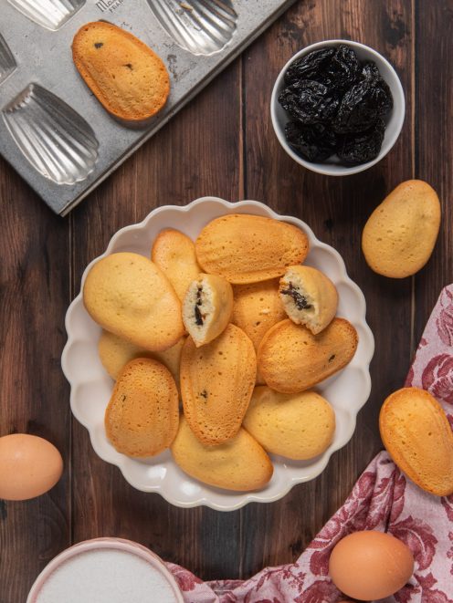 Madeleines con cuore di prugne accatastate in una ciotola, alcune spezzate a mostrare il ripieno