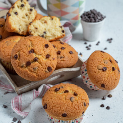 Muffin con gocce di cioccolato disposti su vassoio con uno tagliato a meta e tazza di caffe