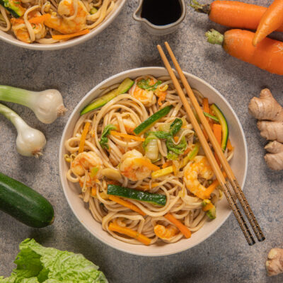 Noodles con gamberi, zucchine e carote saltati, serviti con bacchette