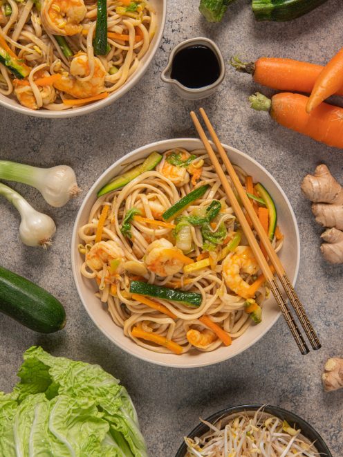 Noodles con gamberi, zucchine e carote saltati, serviti con bacchette