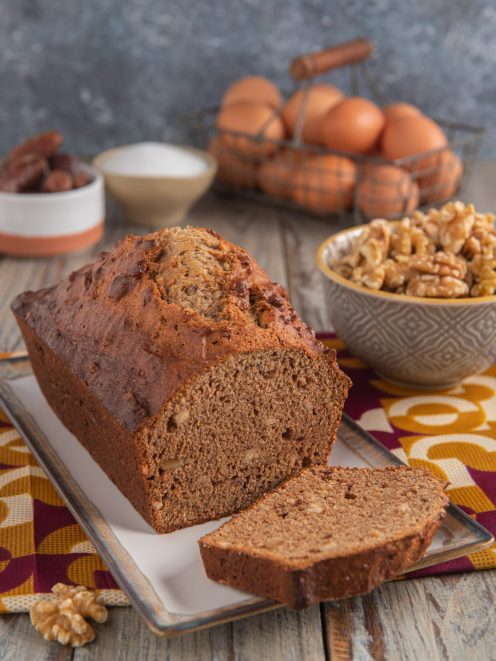 Pane di noci e datteri a filoncino con una fetta tagliata che rivela la mollica compatta