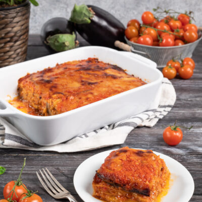 Parmigiana di melanzane appena sfornata con superficie dorata e caramellata, servita a fette