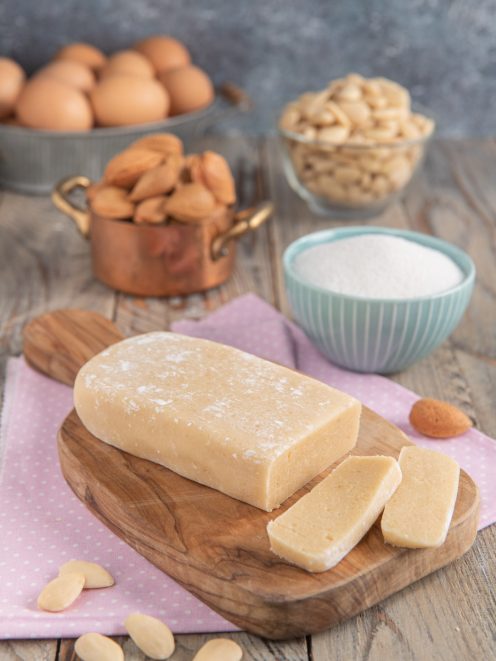 Pasta di mandorle a blocco affettata su tagliere, con mandorle sparse intorno
