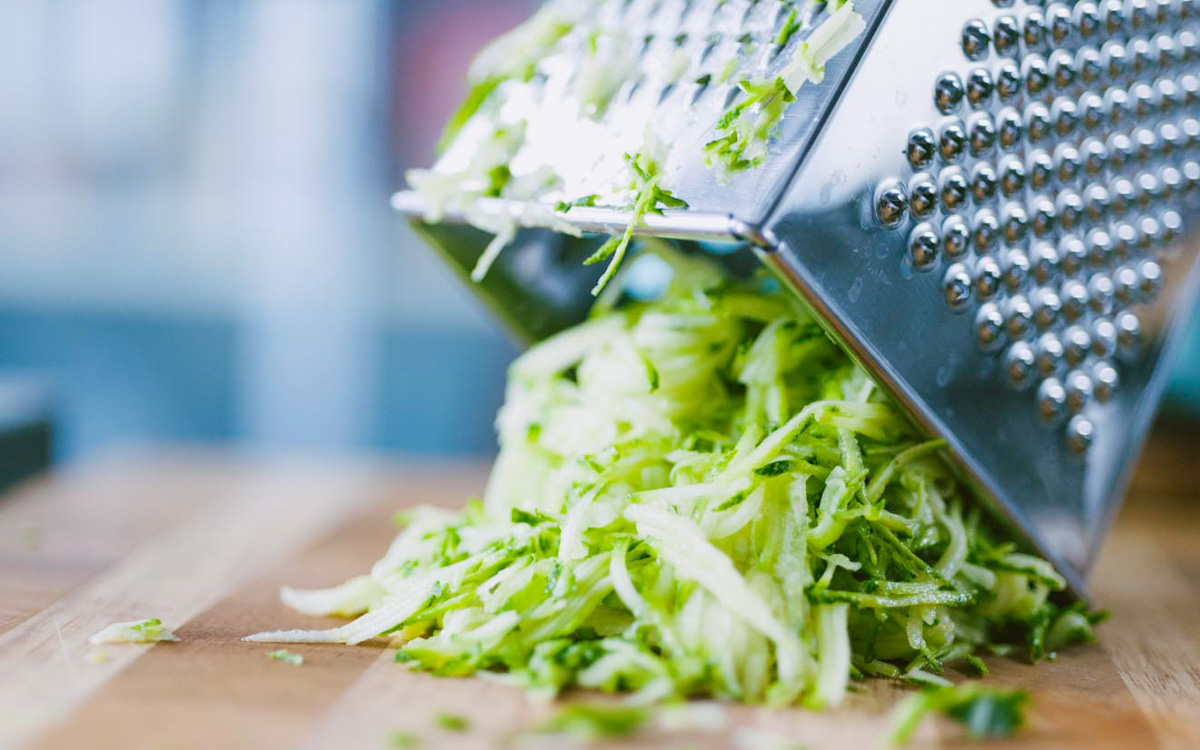 Zucchine grattugiate finemente che cadono dalla grattugia sul tagliere