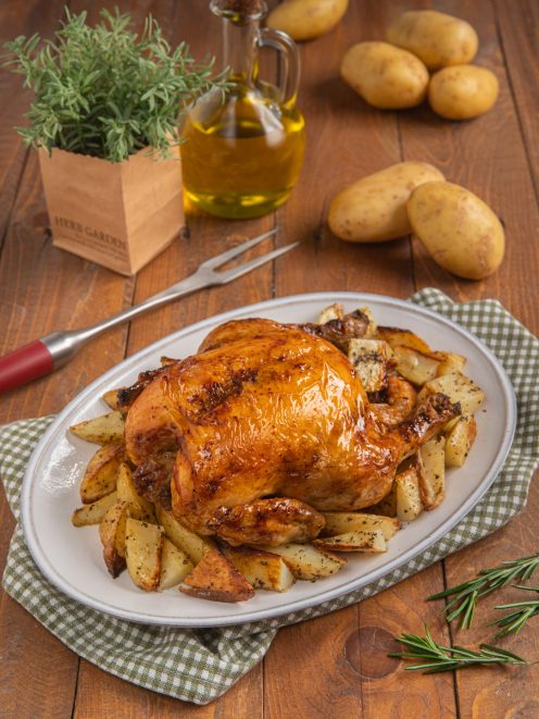 Pollo arrosto intero con pelle dorata e croccante, circondato da patate al forno a spicchi