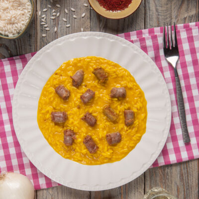 Risotto alla monzese con zafferano e pezzi di luganega distribuiti sulla superficie cremosa