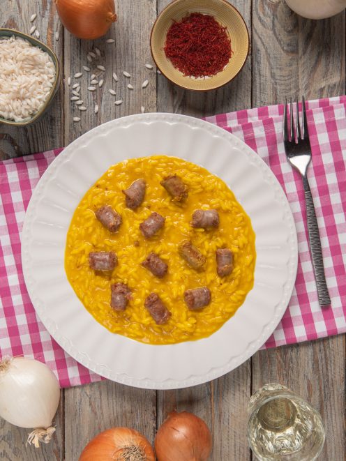 Risotto alla monzese con zafferano e pezzi di luganega distribuiti sulla superficie cremosa