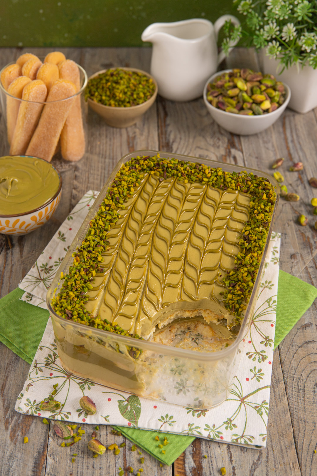 Tiramisù al pistacchio decorato con crema rigata e granella di pistacchi sui bordi, con una porzione già tolta