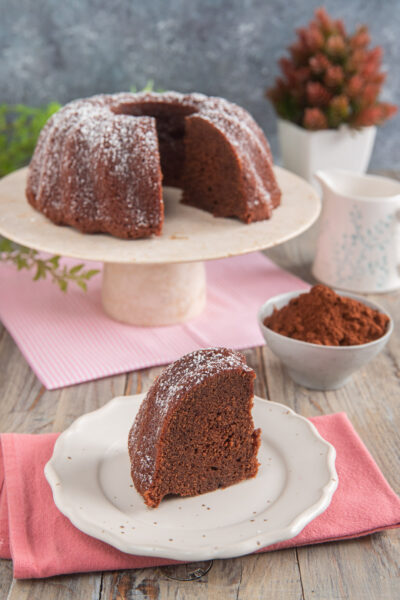 Torta al cacao senza uova tagliata a fette, spolverata di zucchero a velo e servita con cacao amaro
