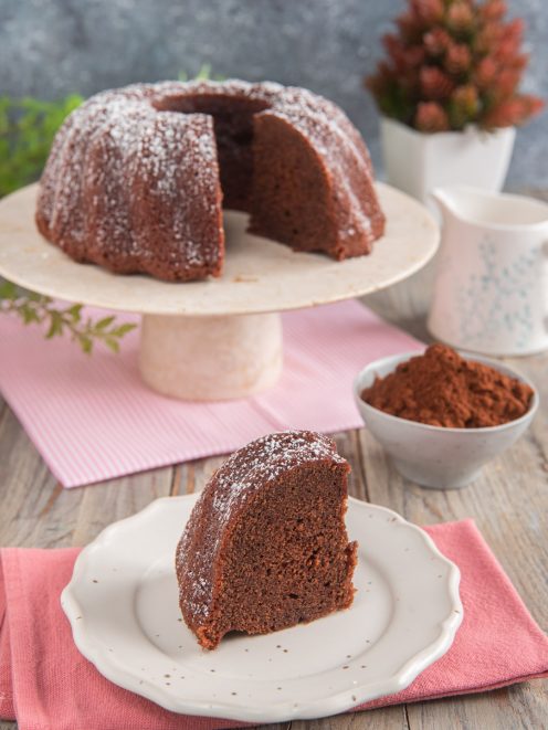 Torta al cacao senza uova tagliata a fette, spolverata di zucchero a velo e servita con cacao amaro