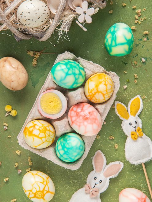 Uova marmorizzate colorate in verde, giallo e corallo su alveolo di cartone tra decorazioni pasquali