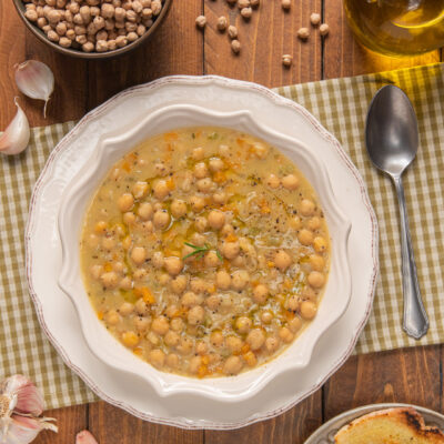 Zuppa di ceci densa con brodo dorato, verdure a pezzi e un filo d'olio, servita con crostini