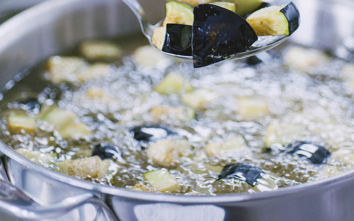 Cubetti di melanzane e zucchine che friggono in olio bollente, sollevati con una schiumarola
