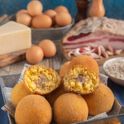 Arancini alla carbonara dorati e croccanti, tagliati a metà per mostrare il ripieno cremoso di riso