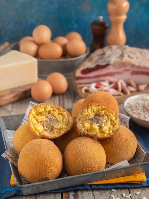 Arancini alla carbonara dorati e croccanti, tagliati a metà per mostrare il ripieno cremoso di riso