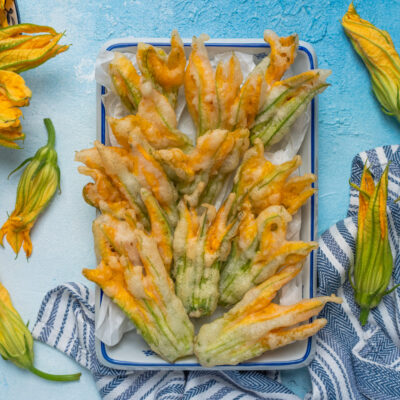 Fiori di zucca in pastella fritti, dorati e croccanti, serviti su carta assorbente