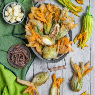 Fiori di zucca ripieni in pastella dorata con mozzarella filante e acciughe
