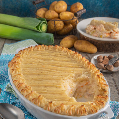 Fish pie gratinato con copertura di purè decorata, porzione che rivela ripieno di pesce e verdure