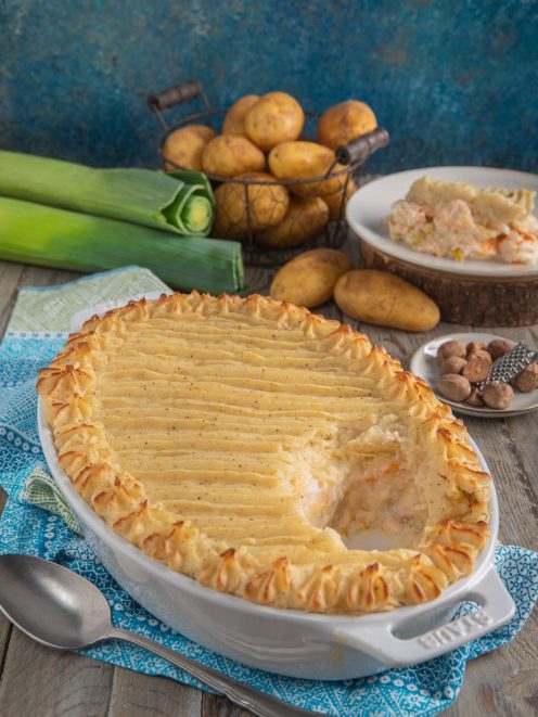 Fish pie gratinato con copertura di purè decorata, porzione che rivela ripieno di pesce e verdure
