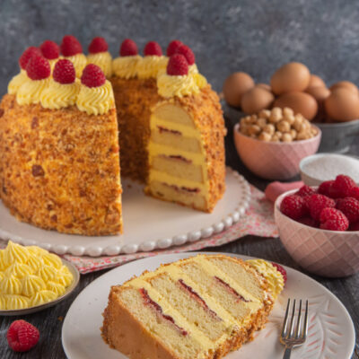 Frankfurter Kranz a strati farciti di confettura e crema al burro, ricoperto di granella e lamponi freschi