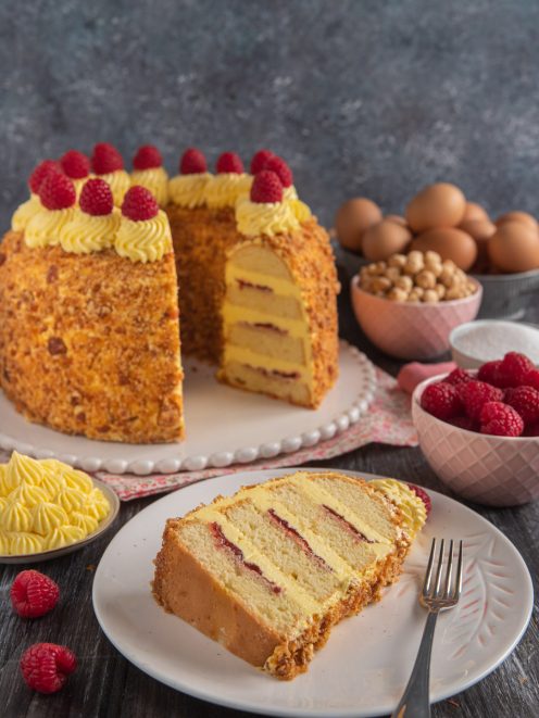 Frankfurter Kranz a strati farciti di confettura e crema al burro, ricoperto di granella e lamponi freschi