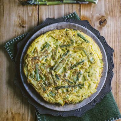 Frittata di asparagi dorata con pezzi di asparagi verdi ben visibili, servita intera
