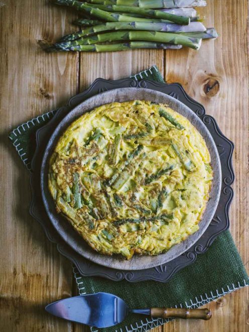 Frittata di asparagi dorata con pezzi di asparagi verdi ben visibili, servita intera