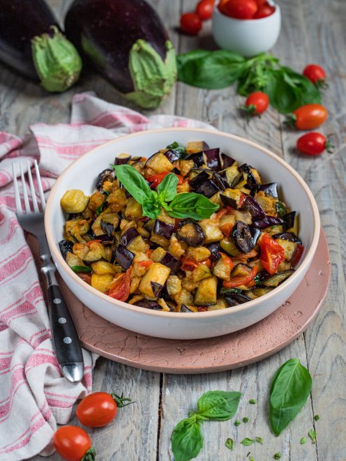 Melanzane a funghetto con pomodorini e foglie di basilico fresco