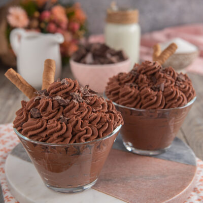 Mousse al cioccolato servita in coppa con ciuffi di crema, scaglie di cioccolato e un wafer